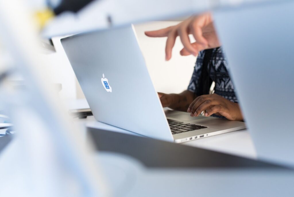 a photo showing the back of a laptop, with a hand pointing at a screen.