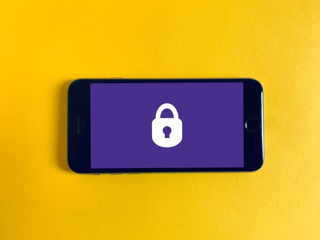 A photo of a mobile phone on a yellow background. The screen shows a lock to represent cybersecurity